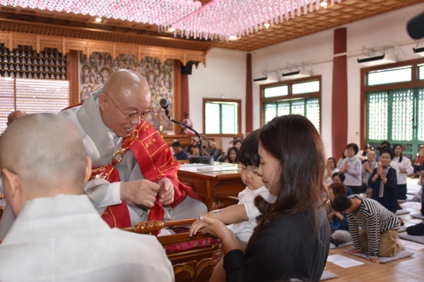 총무원장 상진 스님이 한 어린 아이에게 연비의식으로 보살상이 새겨진 티켓을 팔에 부쳐준 후 합장주를 채워주고 있다.